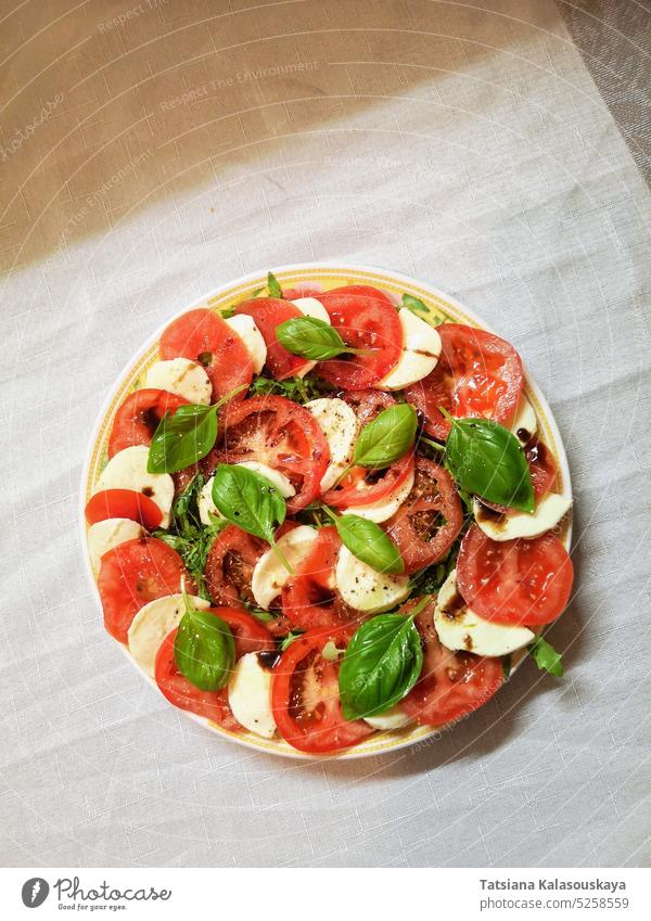 Top view of a plate with fresh Italian caprese salad of tomatoes, mozzarella and basil leaves, dressed with balsamic vinegar and olive oil plan Plate Fresh