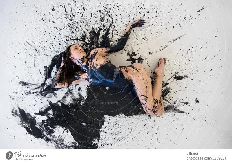 view from above to graphic image of young artistic abstract painted nude sexy woman with black paint, lying on the black and white designed floor in the studio