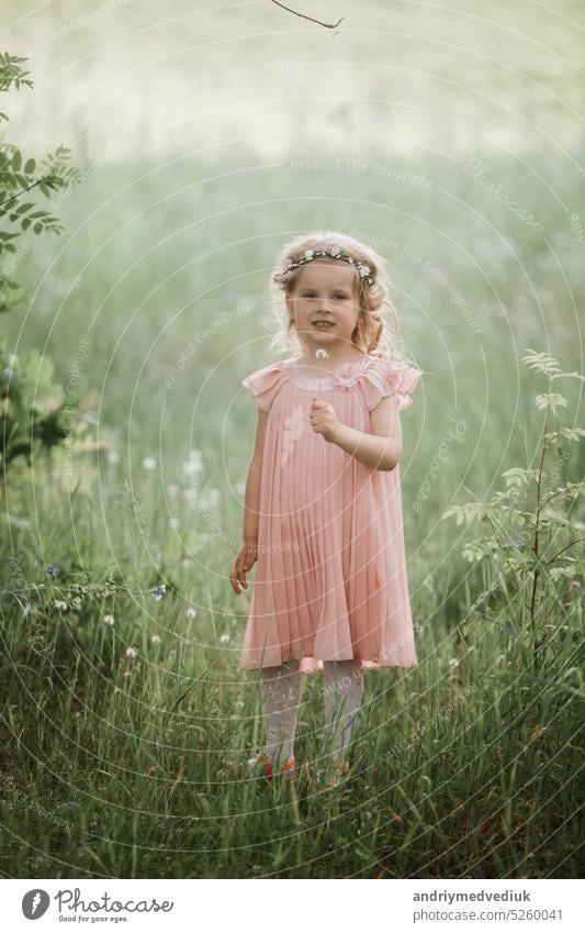 little cute girl in a pink dress and a wreath of flowers on her head walks in the forest in the summer lifestyle spring female portrait caucasian childhood