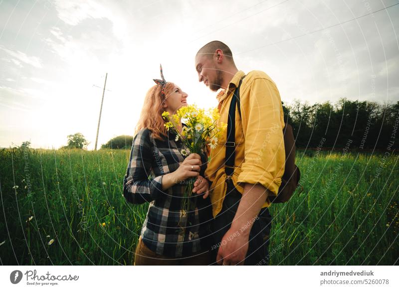 bouquet of wildflowers in woman's hand. Loving hipster couple walking in the field, kissing and holding hands, hugging, lying in the grass in the summer at sunset. valentines day