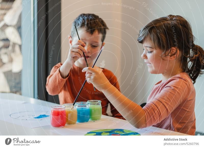Kids creating environmental placards together children paint wash paintbrush creative poster water sibling happy kid table cup childhood friend boy girl brother