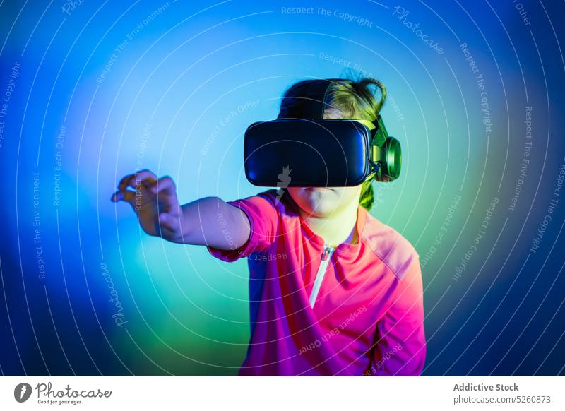 Girl experiencing VR headset game on colorful blue background kid girl touch invisible object vr goggles futuristic cyberspace child connection entertain
