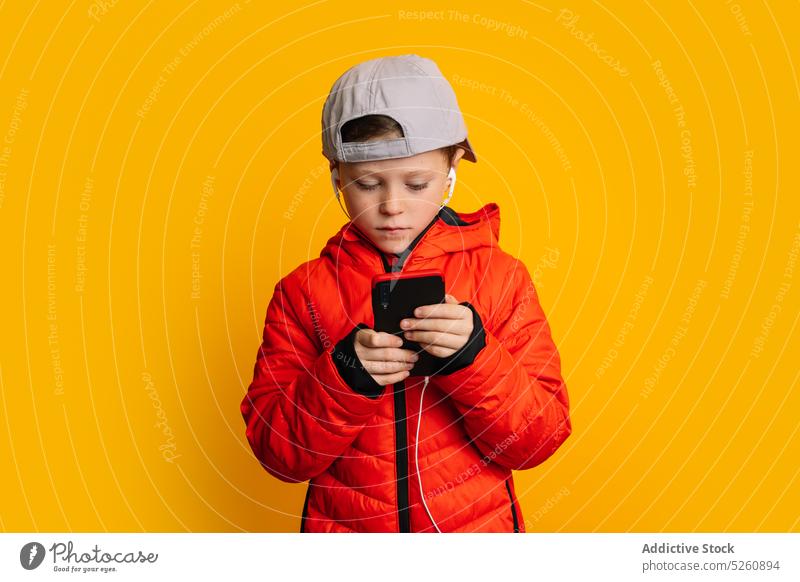 Boy using smartphone and listening to music on earphones kid boy gadget studio shot playlist child song browsing surfing internet wireless connection pastime