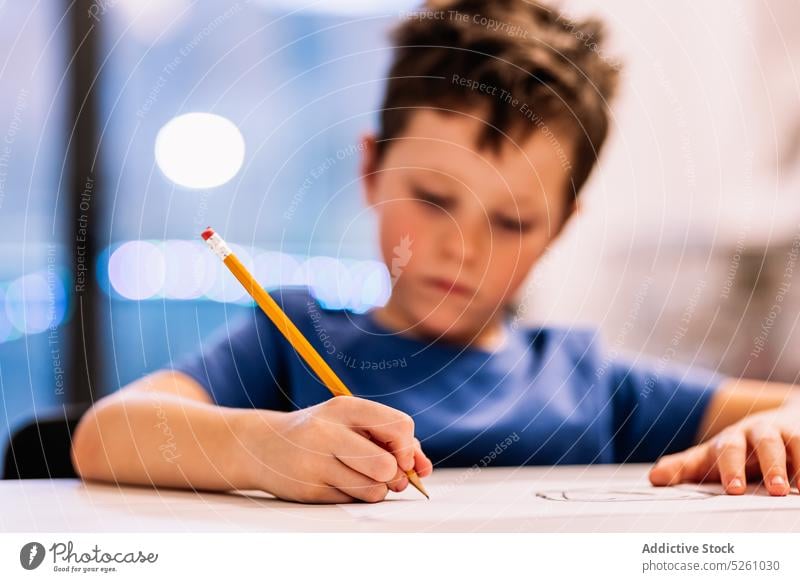 Boy sitting at table and drawing boy home window creative hobby evening child glad childhood kid pencil sketch cute imagination casual dark hair adorable desk