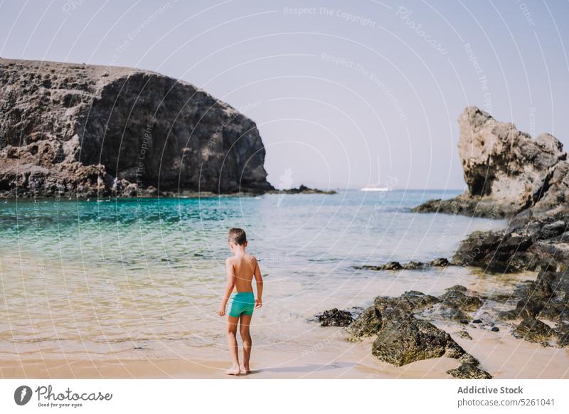 Boy in swim trunks standing on beach child boy sea water shore nature cloudless summer holiday resort kid lanzarote parrot beach spain europe vacation daylight