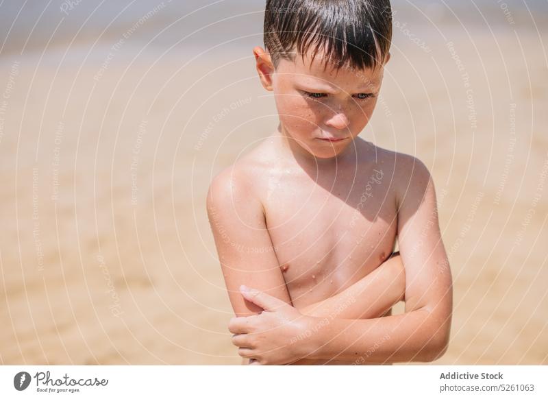 Unhappy boy standing on beach with crossed arms child frown upset sea coast nature resort summer arms crossed displease frustrate problem mood sad unhappy kid