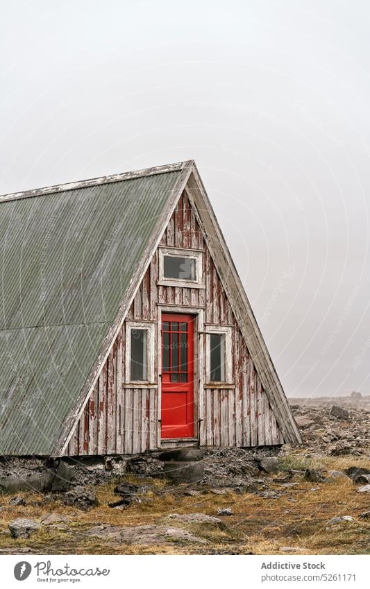 Old wooden triangle house on cloudy day building exterior facade shabby terrain gloomy construction cottage rocky door old structure aged weathered rural
