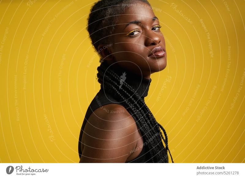 Serious African American woman near yellow wall arrogant makeup vivid bright hairstyle braid appearance fashion ethnic female top cool confident serious