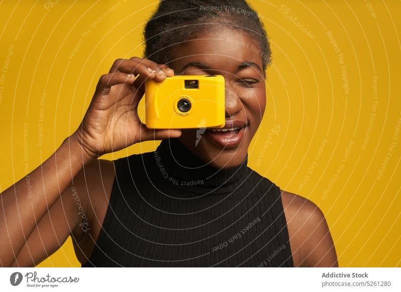 Cheerful African American woman with retro camera on yellow background cheerful take photo photo camera photography capture vivid bright hobby photographer
