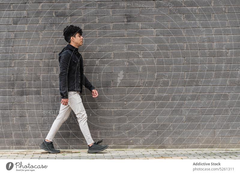 Young male migrant walking on street near brick wall man student independent building immigrate opportunity unemotional guy hispanic ethnic latin american