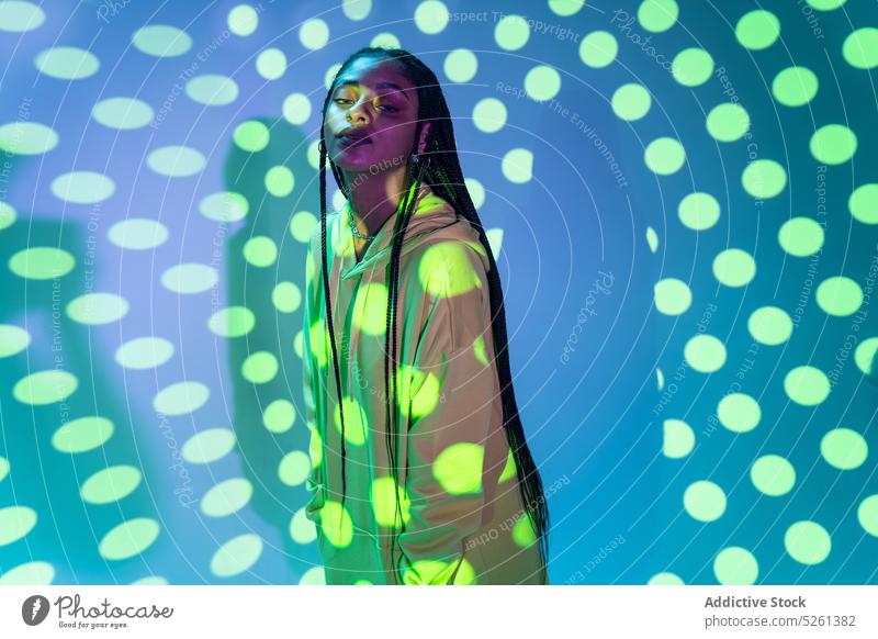 Black female model standing against glowing polka dot projector woman pattern neon illuminate light effect emotionless unemotional african american portrait