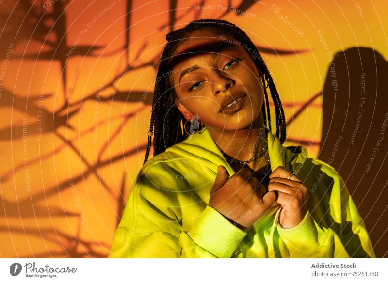 Black female touching chain standing in studio against orange light woman model portrait geometry personality neon confident african american black ethnic young