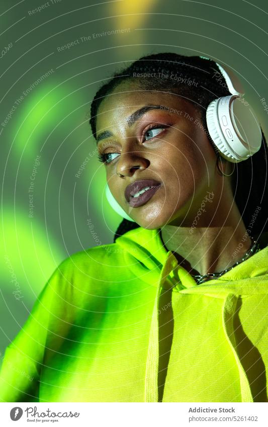 Black woman touching headphones while standing in studio with neon lights model sound listen music projector female african american black ethnic young