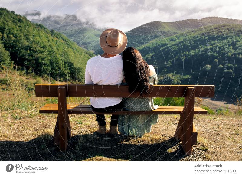 Happy couple sitting on bench in mountains rest close admire love romantic amorous date young happy together dress daytime fondness holiday harmony gentle