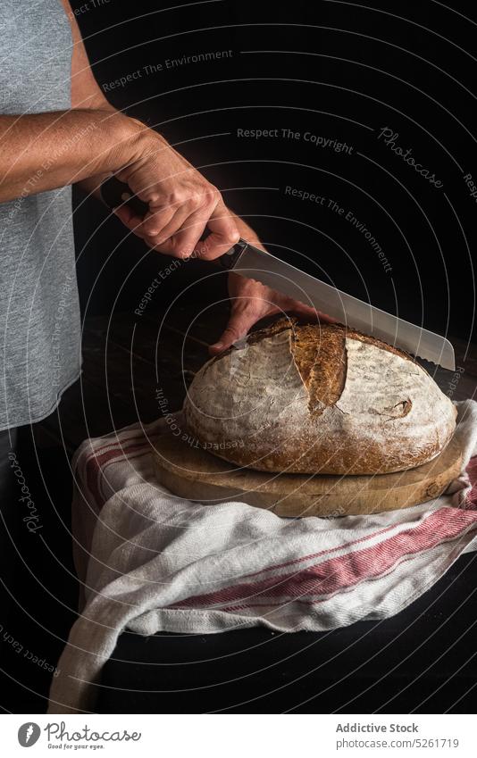 Crop person cutting bread with knife loaf artisan sourdough baked rye whole cutting board baker organic natural homemade fresh food culinary product towel