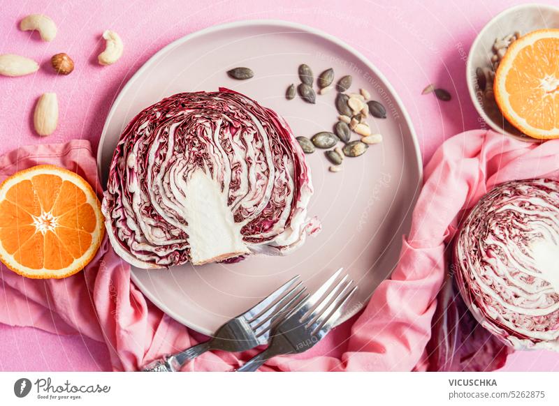 Halved radicchio with salad ingredients on plate at pink table background, top view. Healthy food concept halved healthy food above vegan cooking purple lettuce
