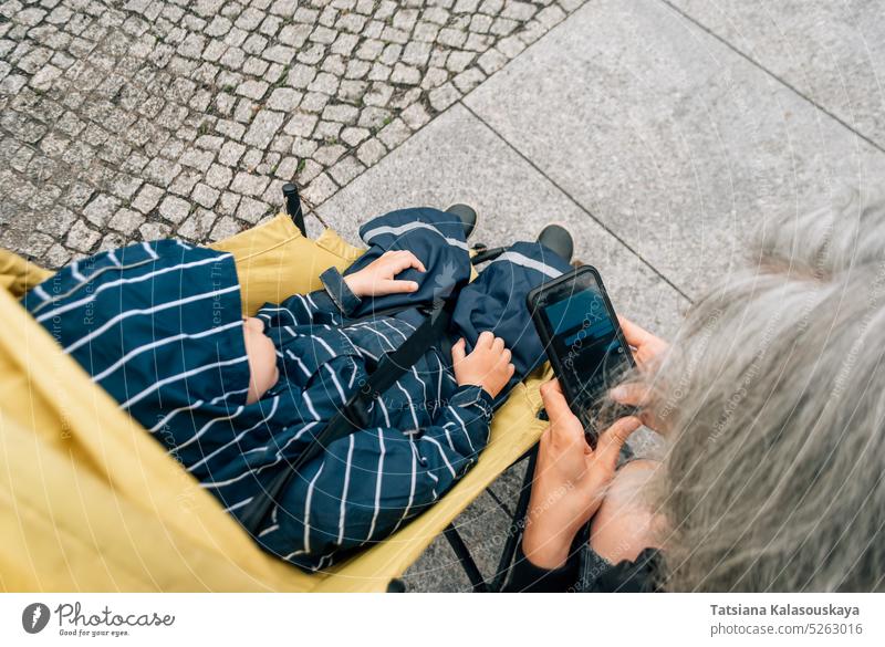 Top view of a woman typing a message on her phone, near a stroller with a child boy son mother motherhood childhood parent female family parenting mother figure
