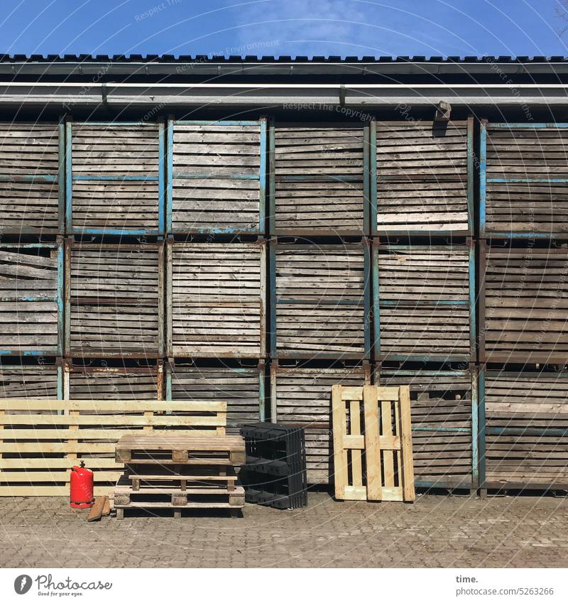 Gas bottle next to pallets in front of storage shed on paving stones in sunlight under blue sky gas cylinder Palett Wooden pallets Storage shed Paving stone