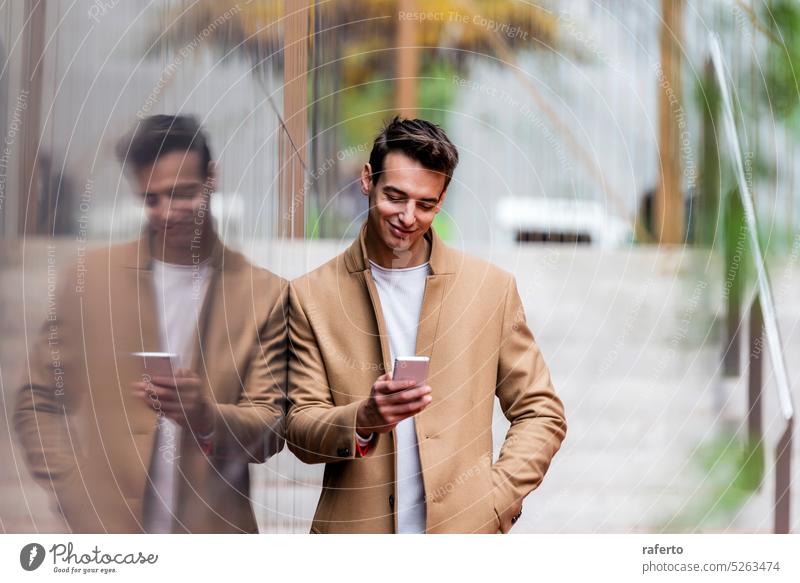 Portrait of stylish handsome young man with coat standing outdoors and leaning on wall using a smartphone Adult Camera Caucasian Confidence Elegance Inspiration