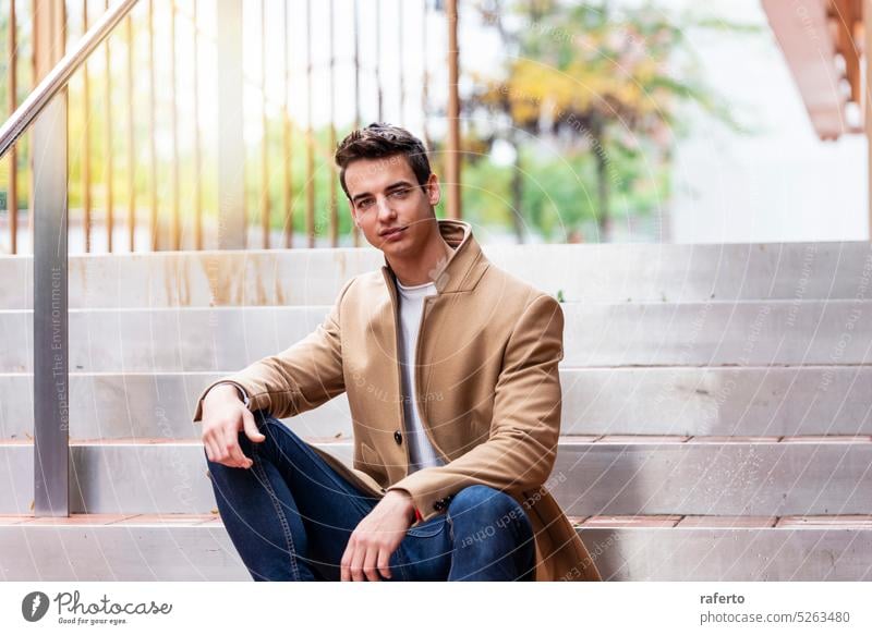 Portrait of stylish handsome young man with coat sitting outdoors Adult Camera Caucasian Confidence Elegance Inspiration Jacket Leaning Lifestyle Male Modern