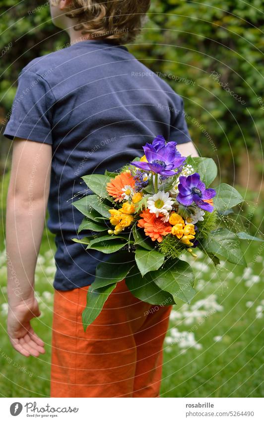 Child hides bouquet of flowers behind his back Bouquet Donate give away Surprise KInfant Mother's Day covert Hide hand Green Orange Blue variegated
