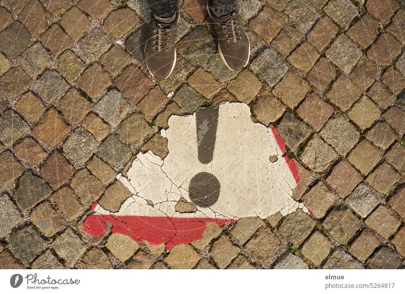 View from above of a peeling traffic sign - Attention General Danger Area - , a person's shoes and old cobblestones Attention General Danger Zone Road sign