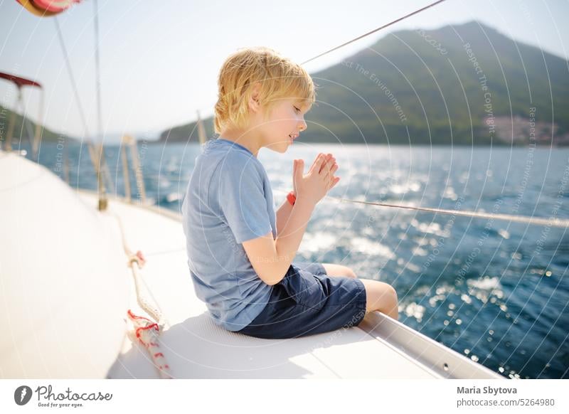Little boy on board a sailing boat in the Boka Kotor Bay of the Adriatic Sea in the Balkan Mountains, Montenegro, Europe. Happy child on a sea trip during the sunny summer holidays day.