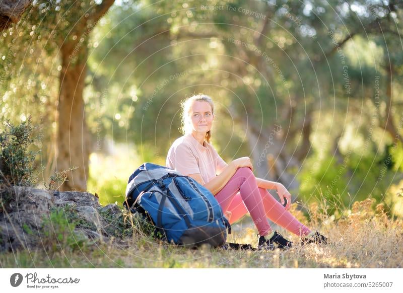 Young woman hiking in countryside. Girl resting under olive tree. Concepts of adventure, extreme survival, orienteering. Backpacking hike relax backpacker