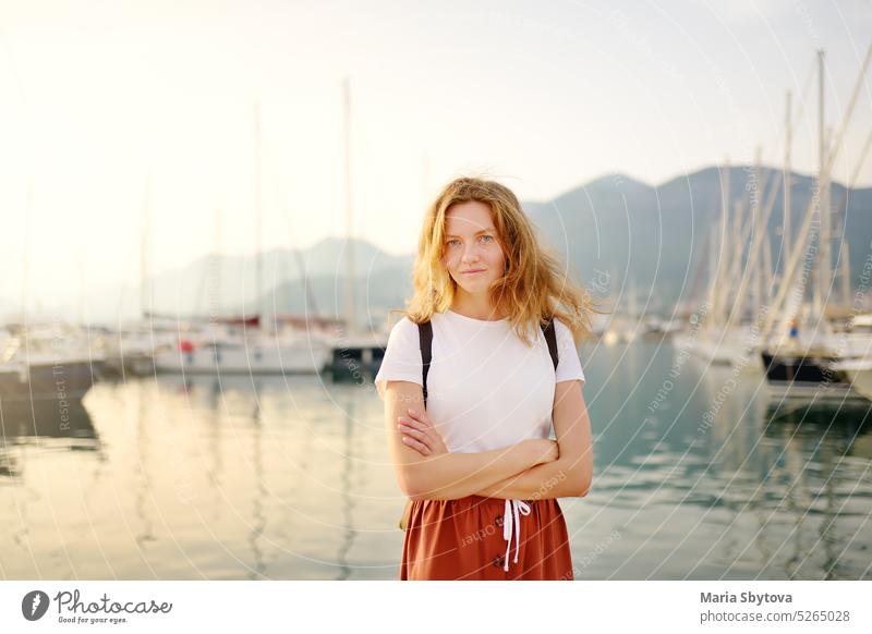 Charming young tourist woman travel by Mediterranean coast. Attractive red-haired girl on the background of sea and yachts. Yacht rental. Tourism and travel