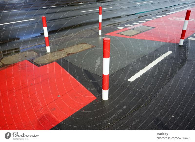 Road marking in red and white on gray asphalt for the bike lane with bollards after rain in the sunshine on Hanauer Landstraße in the Ostend of Frankfurt am Main in the German state of Hesse