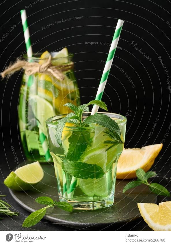 Lemonade in a transparent glass with lemon, lime, rosemary sprigs and mint leaves on a black background lemonade drink cocktail refreshment fruit ice green