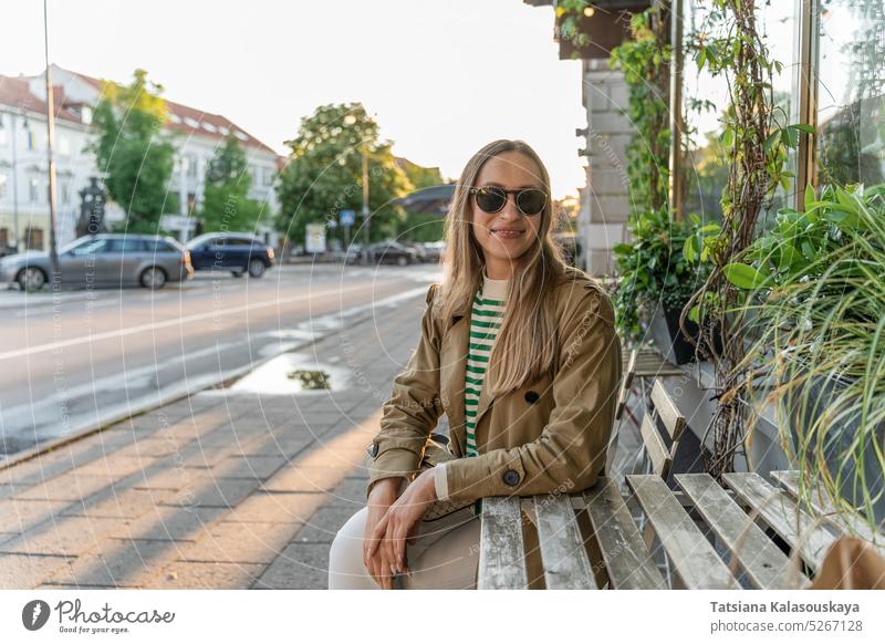 A woman in sunglasses sits at the table of an outdoor cafe female joy adult smile Contented Confidence smiling real life Lifestyle Positive Optimistic