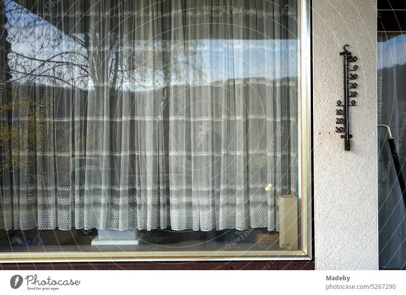 Curtain in an old window with frame made of brass and outside thermometer of a former gas station in beige and natural colors at the Edersee near Waldeck in the district of Waldeck-Frankenberg in Hesse, Germany