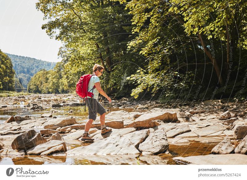 Trekking with backpack concept image. Female backpacker wearing trekking boots crossing mountain river. Woman hiking in mountains during summer trip adventure