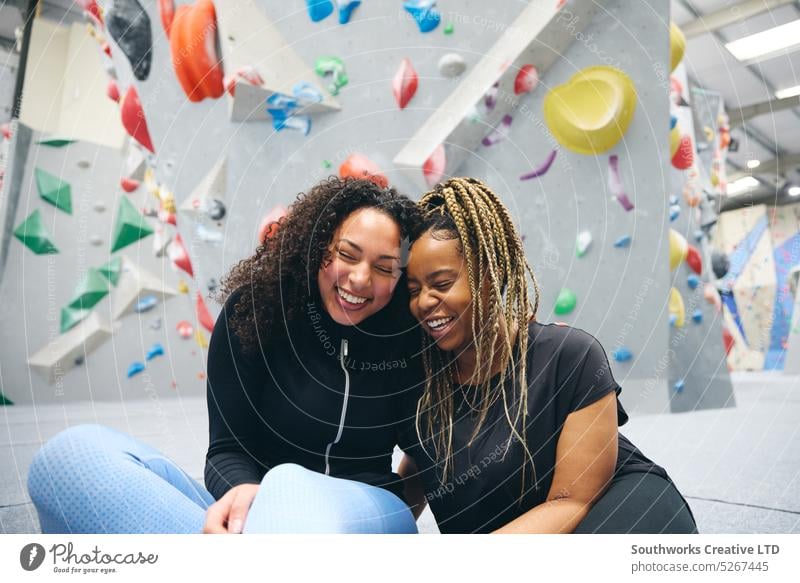 Two Smiling Female Friends Having Fun Laughing As They Try Climbing Wall At Indoor Activity Centre women friends climber climbing center centre indoors wall