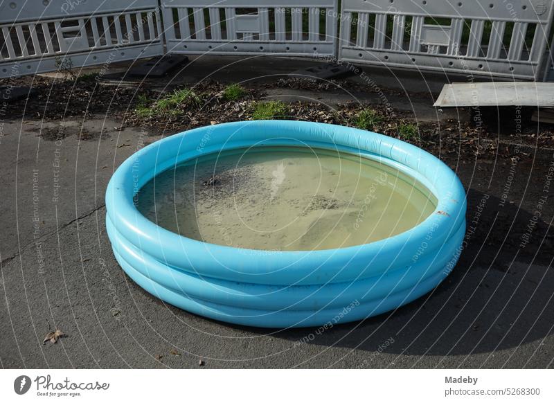 Inflated blue round paddling pool with sand and water on gray asphalt on a construction site with barrier in springtime sunshine in the city center of Wuppertal in North Rhine-Westphalia, Germany