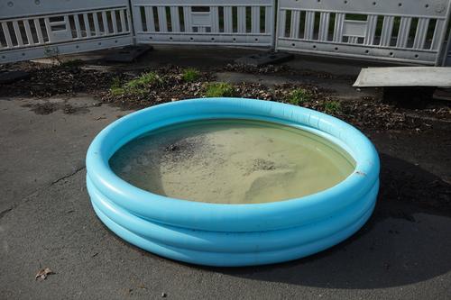Inflated blue round paddling pool with sand and water on gray asphalt on a construction site with barrier in springtime sunshine in the city center of Wuppertal in North Rhine-Westphalia, Germany