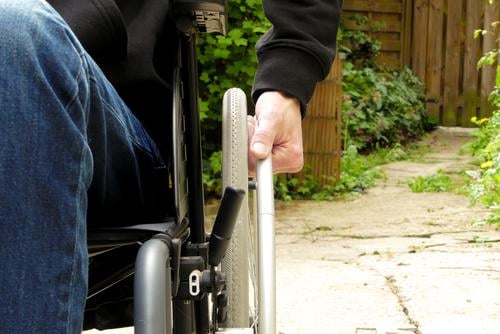 A disabled person in a wheelchair. A man with reduced mobility in an alley with vegetation. alone disabilities disability outdoors hand close up