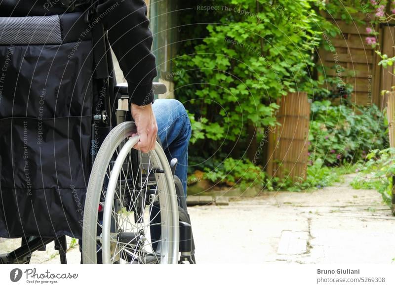 A disabled person in a wheelchair. A man with reduced mobility in a path with vegetation. disability persons with disabilities physical disability garden