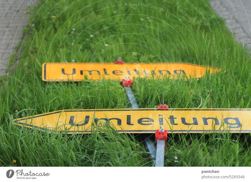 two detour signs, road signs, lie in the meadow and point in opposite directions. confusion Diversion Road signs Signs Road traffic traffic guidance