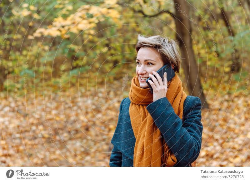 Short-haired blonde smiles as she talks on the phone in the fall outdoors woman autumn Call mobile mobile phone communication On the phone leaves fallen leaves