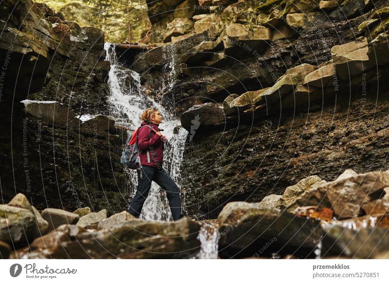 Hiking in mountains. Woman enjoying hike on sunny vacation day. Female with backpack walking close to waterfall. Spending summer vacation close to nature trip