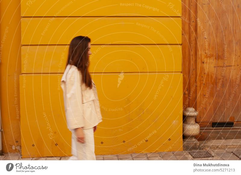 Young woman walking past yellow building. Motion blur image. Person moving in the city. millennial urban model fashion wall tourist tourism young adult shy