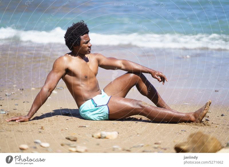 Black man in swimsuit sitting on sandy beach sea seashore summer vacation relax holiday water weekend male ethnic african american black coast wave guy daytime