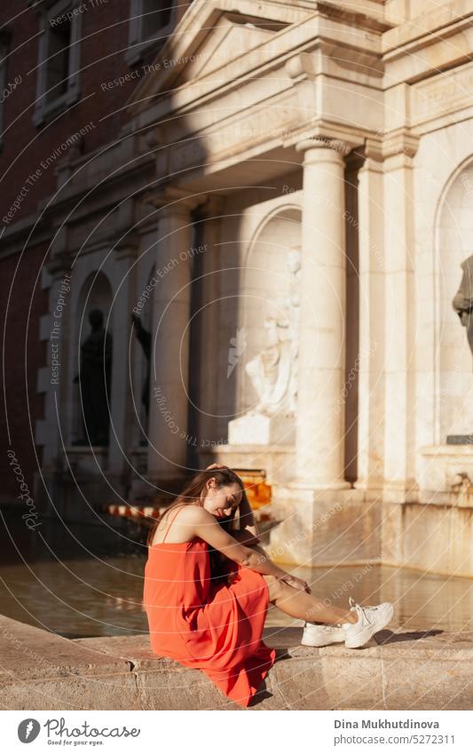 young woman in red dress sitting near fountain. Female tourist posing for photoshoot. Fashion and style. Tourism Tourist travel outdoors lifestyle summer