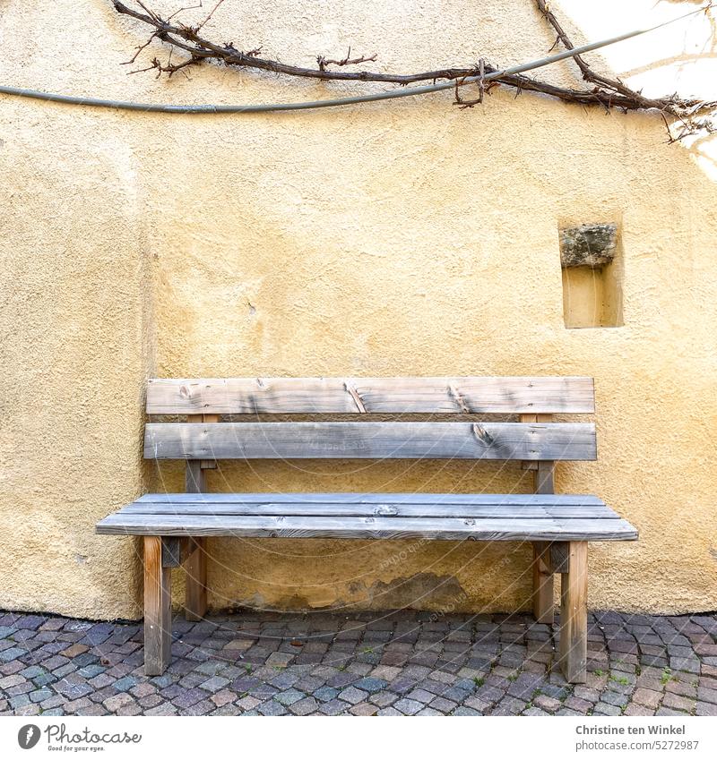 A weathered wooden bench in front of a yellow painted wall Wooden bench seat Rendered facade Cobblestones Wall (building) yellow wall Plaster Old Weathered