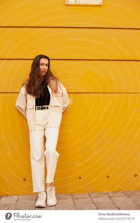 Young woman standing near yellow wall looking in the camera millennial urban model fashion city tourist tourism young adult shy angry attractive annoyed bored