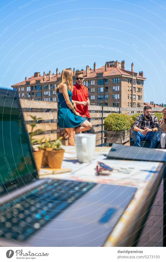 Couple talking in coffee break on office rooftop next to their colleagues couple partner terrace business businesspeople teamwork group pause laptop workplace