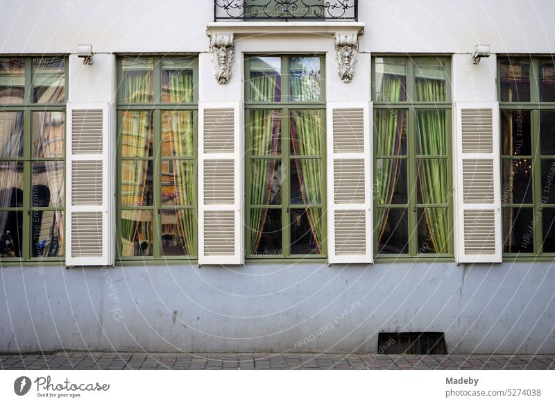 Beautiful green old windows with matching color curtains and wooden shutters with slats of a renovated old building in the old town of Ghent in East Flanders in Belgium