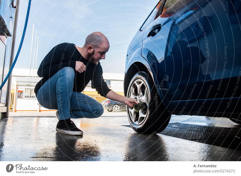Young man cleaning the tire of his car with a sponge at a carwash Car wash tyre dirty Cleaning Dirty Wash water automobile Car wash service Vehicle work Foam